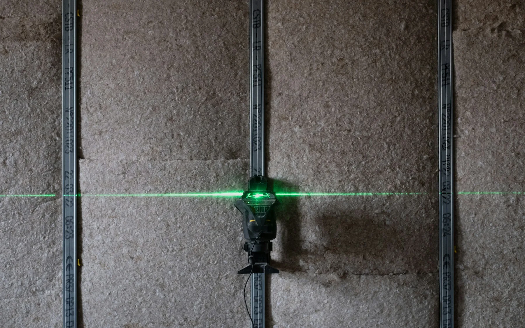 Linie laser verde pe perete de gips, sculă prinsă pe profil metalic, treabă de aliniere